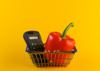 Mini Shopping basket with bell pepper and calculator on yellow background. Calculation of the cost of purchases in supermarket, economy.