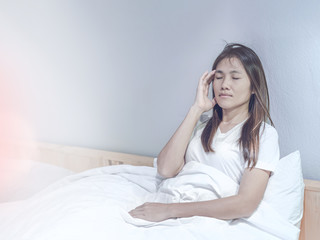 Young asian woman feeling headache and discomfort on white bed in her bedroom.