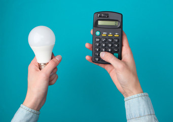 Eco, save energy concept. Female hands hold calculator and light bulb on blue background. Top view