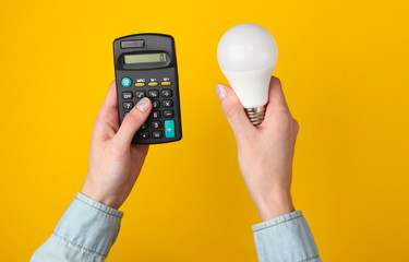 Eco, save energy concept. Female hands hold calculator and light bulb on yellow background. Top view