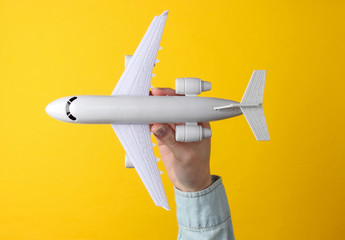 Female hand holds a toy airplane on a yellow background. Travel concept