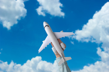 Female hand holds a toy airplane against the blue sky with white clouds. Travel concept