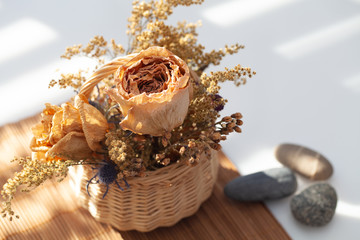 Two dried roses as primary objects, and a variety of smaller branches with tiny flowers, in a basket. Blurry background highlights the solid texture of roses.
