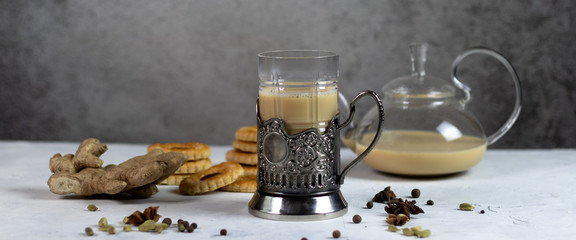 Spicy milk Indian tea Masala in tea cup holder with teapot on the background. Milk, ginger, cardamom, cloves, nutmeg, star anise, cinnamon