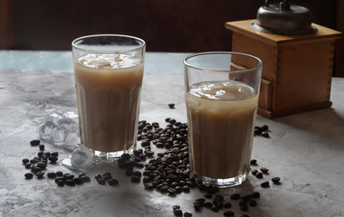 iced coffee in two glass cup and coffee beans  on white table coffee grinder on the background.