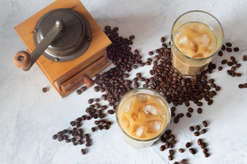 iced coffee in two glass cup and coffee beans  on white background. coffee grinder on the background. top view