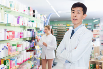 Portrait of chinese man pharmacist who is standing on his work place in apothecary.