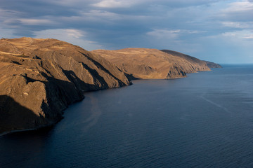 Incredible views of the rocky shore of Lake Baikal. Brown cliffs. There are ripples on the lake. Clouds in the sky.