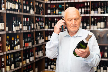 Mature man chooses wine and consults on a cell phone