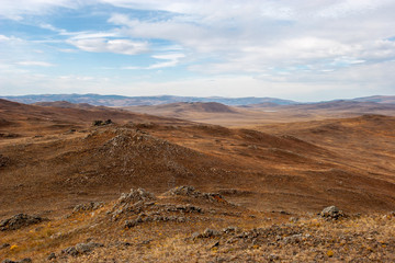 Beautiful steppe landscape with hills and stones in brown tones. Alien landscape. Clouds in the sky.