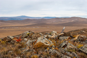 Landscape in a hilly area with rocky stones in the foreground. Evening brown colors. Clouds in the sky.