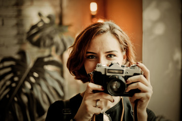 Portrait of a stylish hipster woman with a short haircut with retro camera takes a picture indoors
