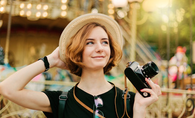 Portrait of young hipster woman in a hat with a retro camera in an amusement park
