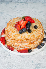 Thin homemade pancakes in a plate with fresh berries and honey.