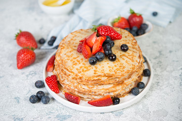 Thin homemade pancakes in a plate with fresh berries and honey.