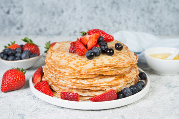 Thin homemade pancakes in a plate with fresh berries and honey.