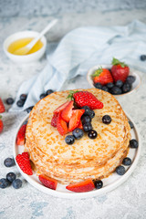 Thin homemade pancakes in a plate with fresh berries and honey.