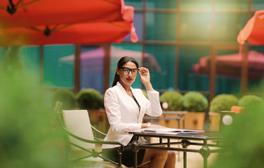 Fototapeta premium Beautiful afro business woman in a white jacket sitting in outdoor cafe