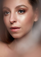 Fototapeta premium Beautiful girl with gentle nude makeup. Young model with shining skin and long hair. Beauty face. Photo is taken in the studio.