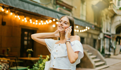 Fototapeta premium Cheerful charismatic woman talking on the phone while walking in the evening along the old city street