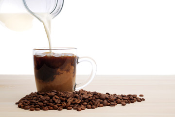 pouring milk into instant coffee in glass mug with roasted coffee beans with copy space