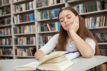 Teenage girl looking tired or bored, studying at the library. Exhausted teen student preparing for exams, reading a book