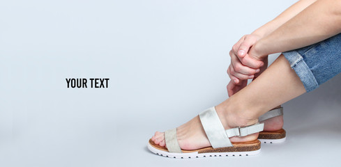 Female legs in jeans and trendy sandals sitting on white background. Cropped Studio Shot. Copy space