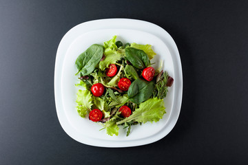 Fresh mixed salad with cherry tomatoes on a black background. Top view.