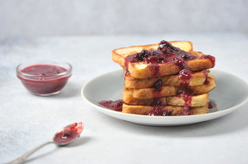 Toast with berry jam on a plate. Near a cup with jam and a spoon. Light background. Close-up. Free space for text.