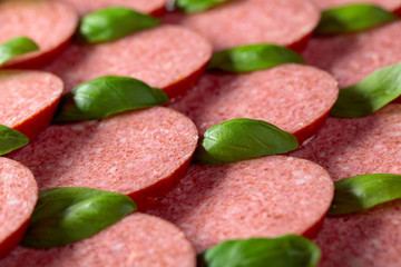 Sliced smoked sausage with green basil leaves.