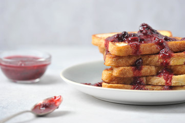 Toast with berry jam on a plate. Near a cup with jam and a spoon. Light background. Close-up.