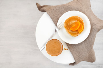 Cup cream coffee or latte, pancakes, fork, tablecloth on a white coffee table. Good morning. Breakfast concept.  Top view. Flat lay