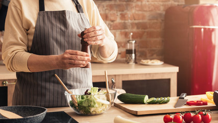 Unrecognizable Aged Woman Holding Pepper Mill Seasoning Vegetable Salad In Kitchen © Prostock-studio