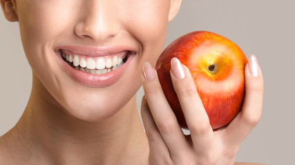 Unrecognizable Girl With Perfect Teeth Holding Apple Smiling, Beige Background