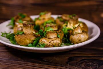 Plate with baked champignons, dill and parsley on a wooden table
