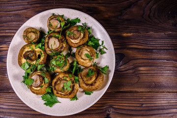 Plate with baked champignons, dill and parsley on a wooden table. Top view