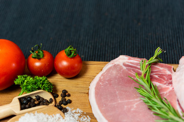 Raw pork chop meat on wood plate with vegetables, spices, salt and black pepper in dark black cloth table