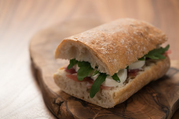 Sandwich with prosciutto, mozzarella and arugula on olive wooden board with copy space
