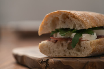 Sandwich with prosciutto, mozzarella and arugula on olive wooden board with copy space