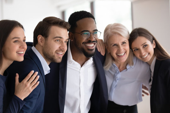 Smiling multiracial businesspeople embrace posing for group picture in office together, happy motivated diverse multiethnic colleagues coworkers show unity and support in work, teamwork concept