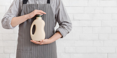 Unrecognizable housewife holding washing detergent bottle over white