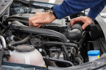 Closeup of mechanic hands checking motor under the hood in the broken car. Repairing of the vehicle concept. Automobile service