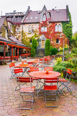 Romantic terrace of outdoor charming street cafe, amazing autumnal scene: wooden furniture at pavement at background of classical Fachwerk architecture. Vertical oriented photo.