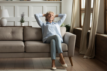 Fototapeta premium Relaxed mature 60s grandmother sit on couch in living room sleep, daydream or take nap, calm senior 70s woman rest relax on comfortable sofa ta home, breathe fresh air, stress free concept