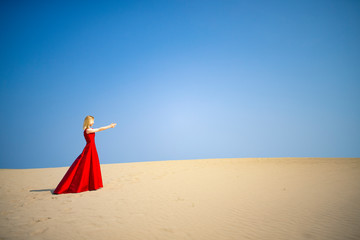 赤いドレスを着て砂丘に立つ白人女性