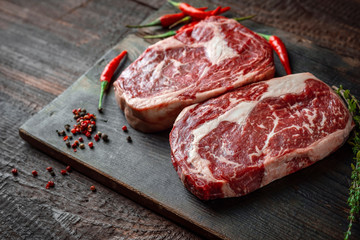 Two classic raw rib eye steaks with red hot peppers on a wooden Board