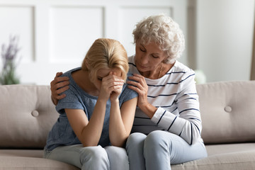 Loving senior mother sit on couch hug depressed millennial daughter suffering from breakup or...