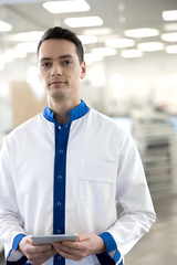 Handsome young man in lab coat holding digital tablet
