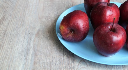 red ripe apples in drops of water on a blue dish on a wooden table 