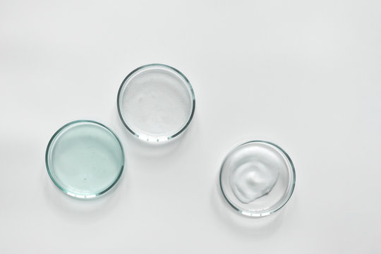 Glass petri dish with different cosmetic products on white background. Shampoo, hair conditioner or mask and shower gel, top view